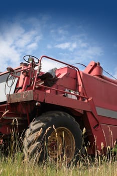 The front end of a red combine harvester machine stationary in a farm field in rural Wiltshire, England, set against a blue summer sky.