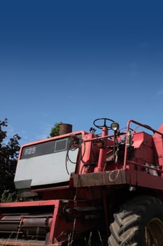 The front end of a red combine harvester machine stationary in a farm field in rural Wiltshire, England, set against a blue summer sky.