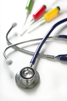 Medical still photo with blue stethoscope and colorful syringe over white