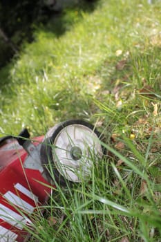 A red lawnmower set amongst long green grass, ready to mow the lawn.