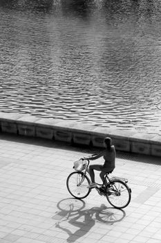 backlit silhouette of girl riding a bike close to park lake, black and white