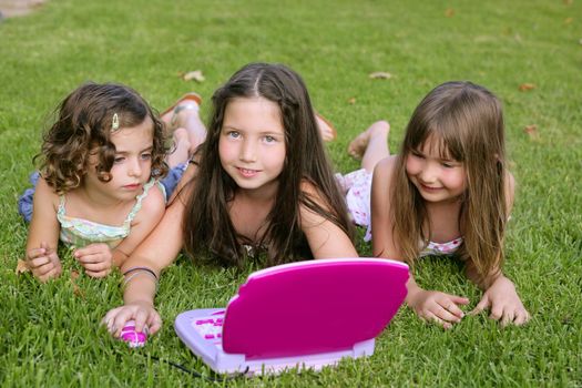 Three little girl outdoor playing with toy computer in grass