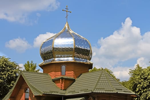 New modern small wooden church with a gilded dome is among the trees. Lviv, Ukraine