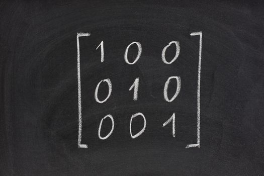 identity matrix with three rows and column handwritten with white chalk on blackboard, eraser smudges texture