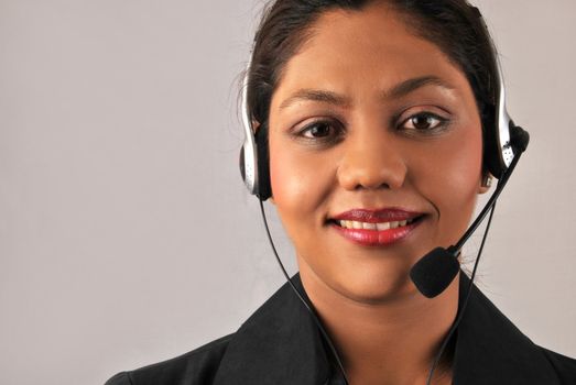 Smiling young Indian agent woman of a call center. Isolated over grey background with copy-space.