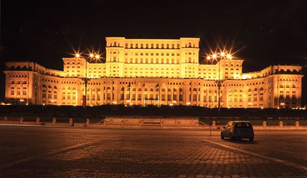 Night image of a car in front of the The Palace of the Parliament, also known as The People's House in the Cheauchesku's era, in Bucharest,Romania. The Palace is the world's largest civilian administrative building, The Pentagon being the largest overall. It is the most expensive and heaviest building in the world.