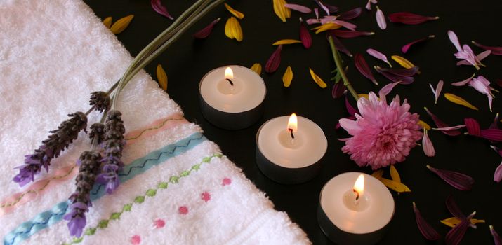 Lavender flowers on a hand towel next to candles with petals spread
