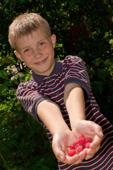 Portret of little smiling boy with raspberry in hands  outdoors