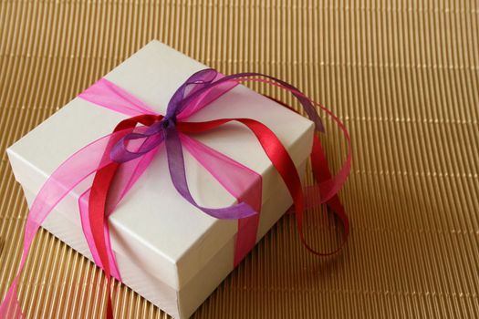 Gift box with pink, purple and red colored ribbons
