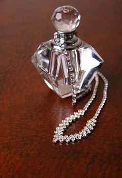 Diamond necklace on a leather surface next to an empty perfume bottle