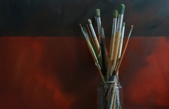 A glass jar of artists brushes set against a grunge styled backdrop.