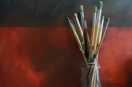 A jar of artists brushes set against a grunge styled backdrop. Set of centre to main image.