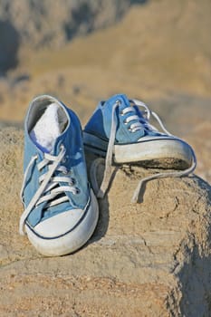 A pair of trainers/gym/beach shoes on top a rock at the beach.