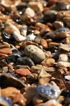 Wet pebbles on a beach. Soft focus to top and bottom of image. Various colours and shapes f pebbles, ideal background image.