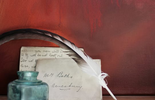 Period set up of a letter,quill pen and glass ink pot set on top of a wooden mantle against a red grunge background. All props recreated by self as artist.