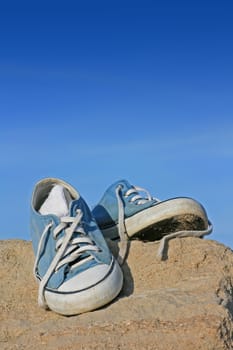A pair of trainers/gym/beach shoes on top a rock at the beach.