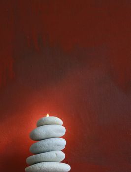 A stack of light grey pebbles stacked on top of eacj other set against a red 'grunge' styled oil painted canvas background. Pebbles have a small flame emerging from its top.