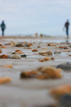 Two figures walking the beach. Sharp focus to mid distance on pebbles and sand, soft focus to foreground and background. Location Christchurch in Dorset UK.