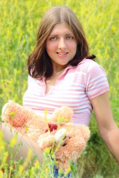 The girl sitting on a summer meadow with a toy bear cub