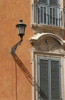 Detailed shot of an italian architecture found in Rome, Italy. Powder blue shuttered windows on a terracotta plaster wall with exterior light casting a shadow.