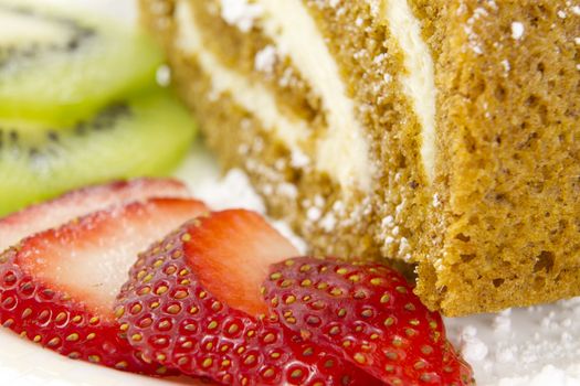 A rolled cake garnished with sliced strawberries and kiwi fruits.