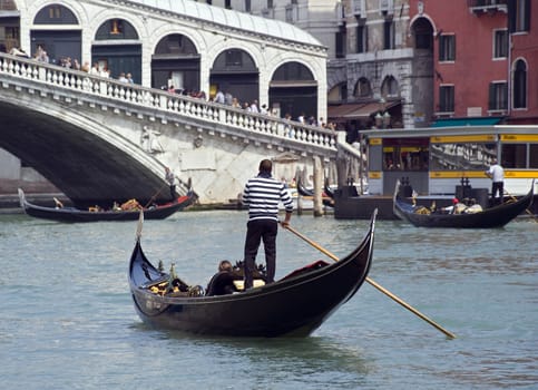A gondolier with tourists in this gondola at the Grand Canal in Venice, Italy. Gondolas are the typical boats in Venice and a tour in such a boat is a highlight of an touristic visit.