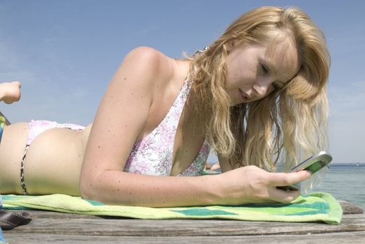 Beatiful blond girl in bikini making call from mobile phone on the beach with blue sky.