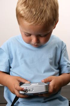 Shy toddler holding a silver camera, looking at his object