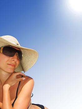 Woman in bikini, hat and sunglasses lying under shinning sun