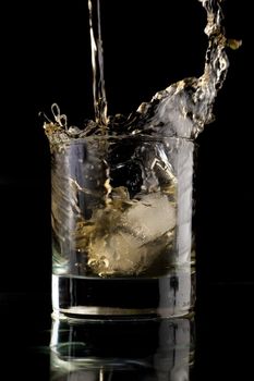 Glass of whisky on a black background. Whisky splash in a glass. Whisky with ice.