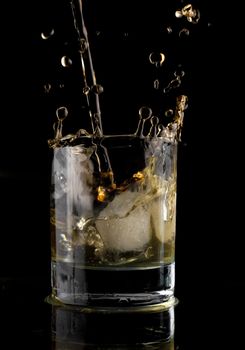 Glass of whisky on a black background. Whisky splash in a glass. Whisky with ice.