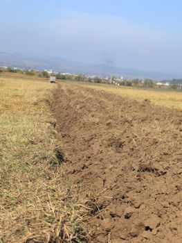 Tilted image of a ploughland with a small tractor in the distance.