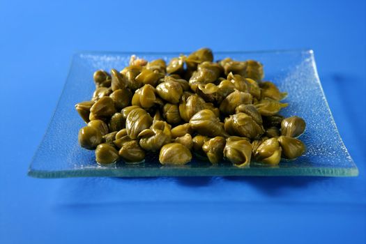 Capers with vinegar snack on a transparent plate, blue background