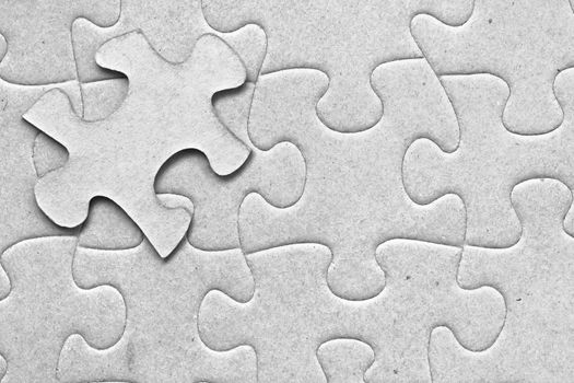 Complete grey cardboard jigsaw puzzle with one floating piece on top