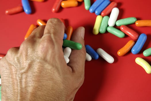 Human man hand holding colorful candy sweets over red