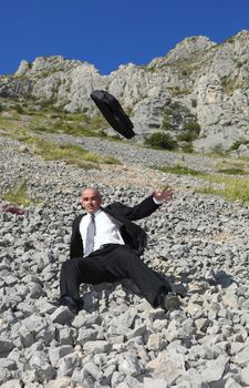 Image of a businessman in a difficult situation sliding on a rocky mountain slope.