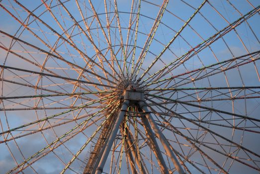 Center of ferris wheel. Spokes radiate outward, deep pink against blue sky
