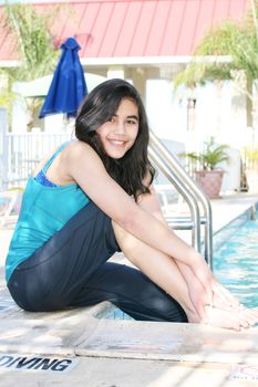 Young teen girl sitting by swimming pool, relaxing