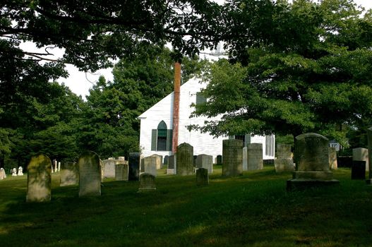 Head stones in cemetery on Maine coastline behind white church