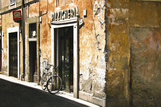 Bicyckle parked in fron of the pizzeria in a ypical italian street