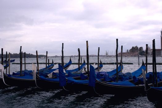 Several gondolas being parked in a venetian lagoon