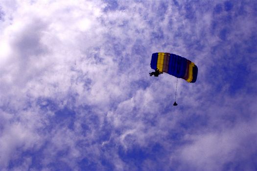 Parachutist with bright parachute soaring in the cloudy sky