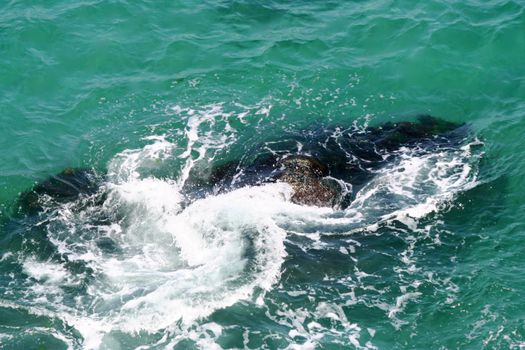 A stone in the turquoise sea with the waves crashig