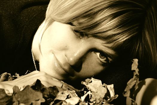 Pretty girl lying on her hands and leaves in the park in autumn