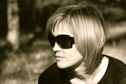 Pretty young woman in sunglasses sitting in the park