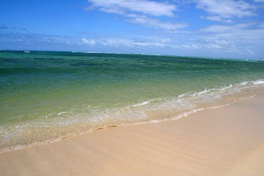 Nice tropical beach with the waves breaking and sun shining through cloudy sky