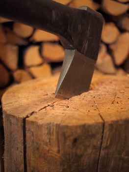 Close-up shot of an axe in a stump with firewood in the background.