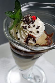 A closeup image of a vanilla ice cream sundae with whipped cream, chocolate covered nuts, chocolate sauce, and a raspberry on top.
