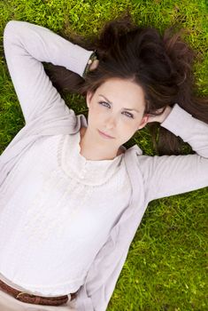 Young attractive woman thougthfully lying in the grass, looking directly in the camera.