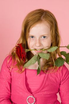 young girl is holding a red rose between her teeth on pink